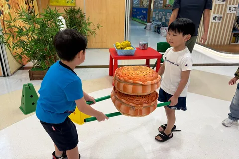 兩位小朋友用兩支棒子合力抬起疊起的月餅抱枕