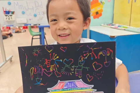 小朋友笑著展示天安門與彩虹煙花的刮畫作品