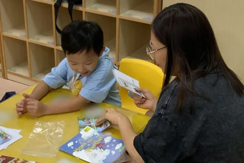 家長在圖書《How’s the Weather?》旁向男孩展示圖卡，男孩開懷大笑
